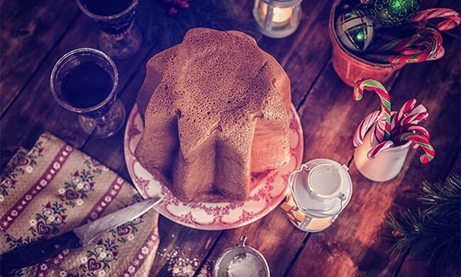 Pandoro visto dall’alto su tavola di legno con addobbi natalizi intorno